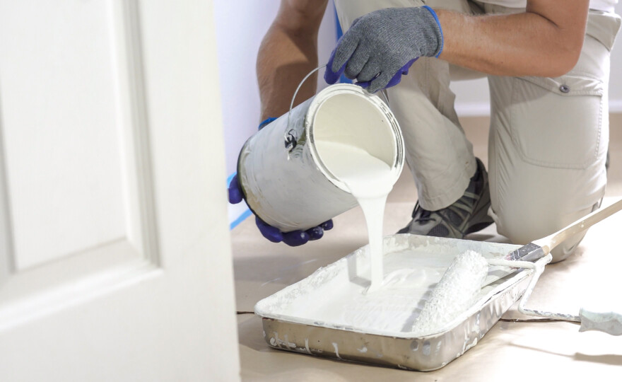 Man pours paint into the tray and dips roller. Professional interior construction worker pouring white color paint to tray.